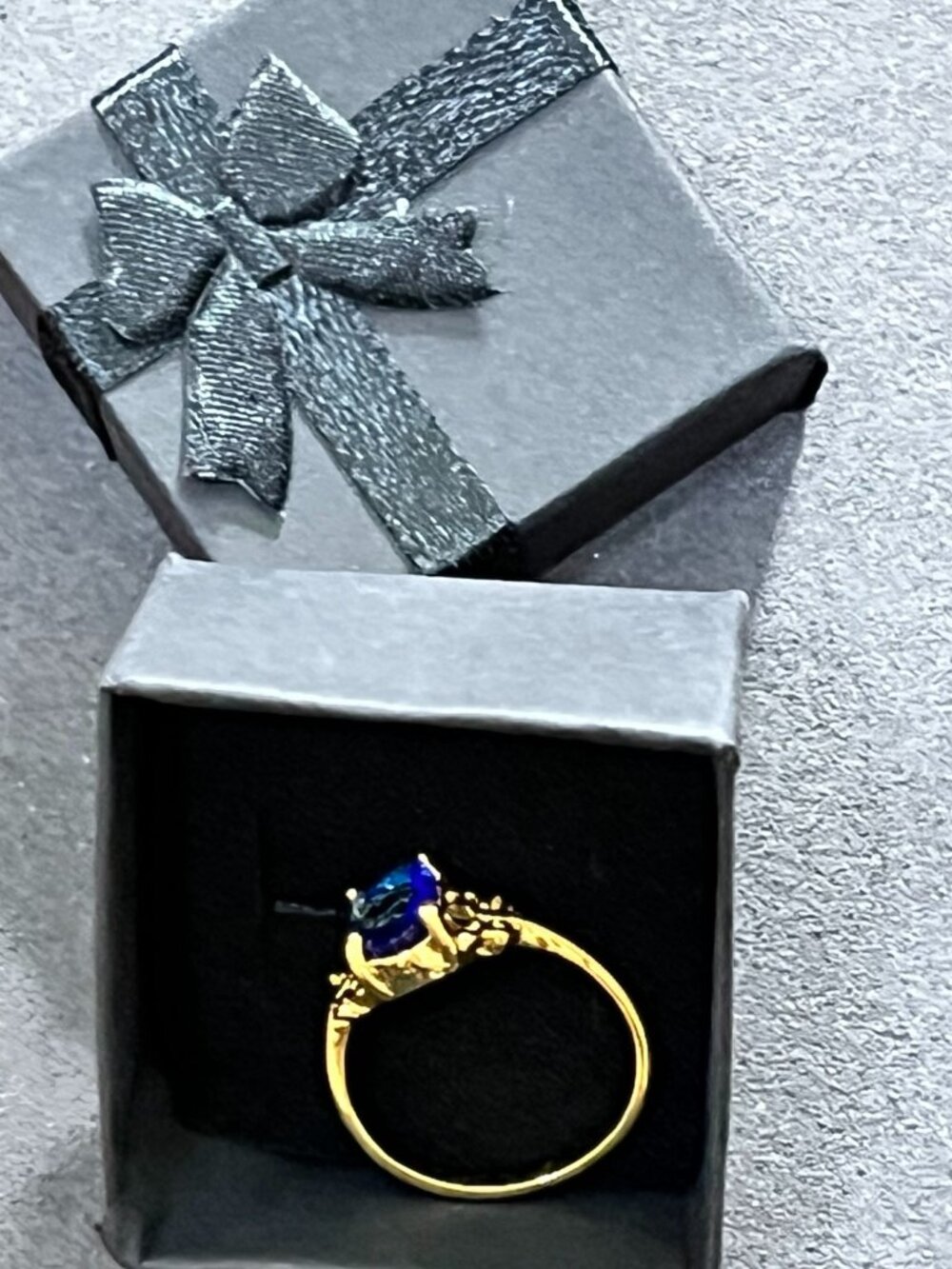 Elegant gold\-tone ring featuring a oval faceted royal\-blue stone with decorati